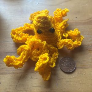 A small yellow crocheted octopus next to a UK penny piece for scale